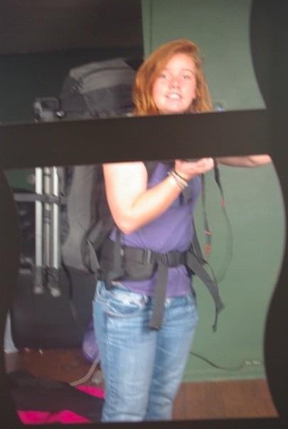 Red haired young woman wearing heavy backpack taking photo in mirror 